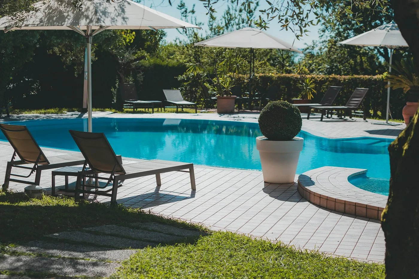 Bordo piscina con lettini, ombrelloni e giardino curato