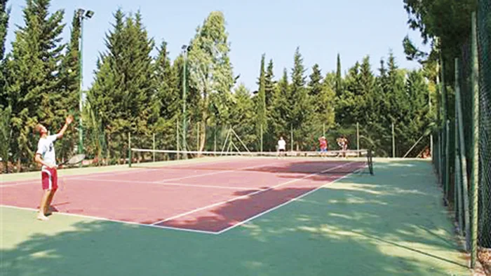 Campo da tennis in terra rossa immerso nella pineta con giocatori in azione