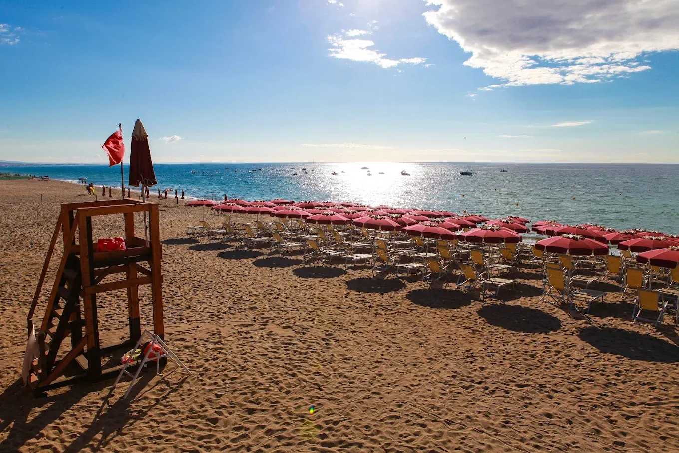 Spiaggia sabbiosa al tramonto con ombrelloni rossi, lettini e torretta di salvataggio