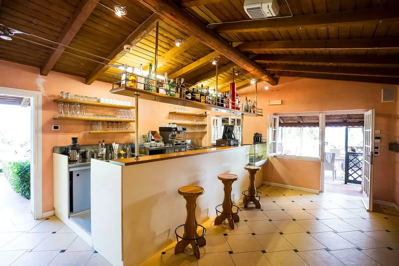 Bar interno con bancone bianco, sgabelli in legno e soffitto in travi a vista