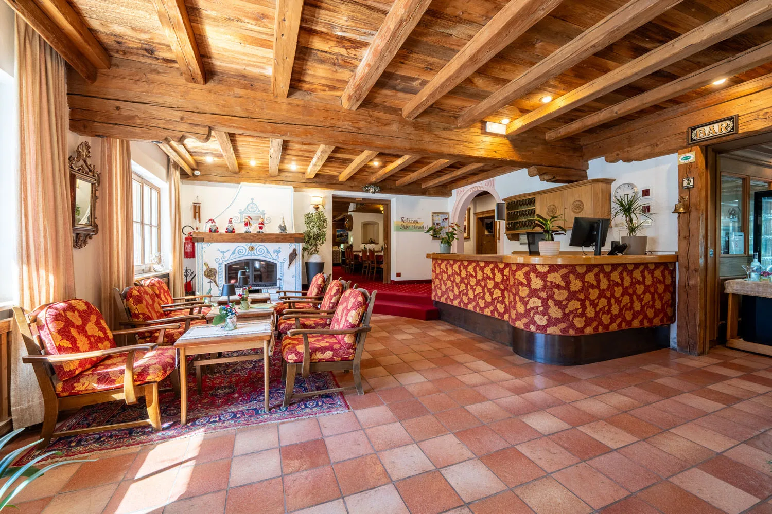 Hall dell'hotel con reception, poltrone rosse e soffitto in travi di legno
