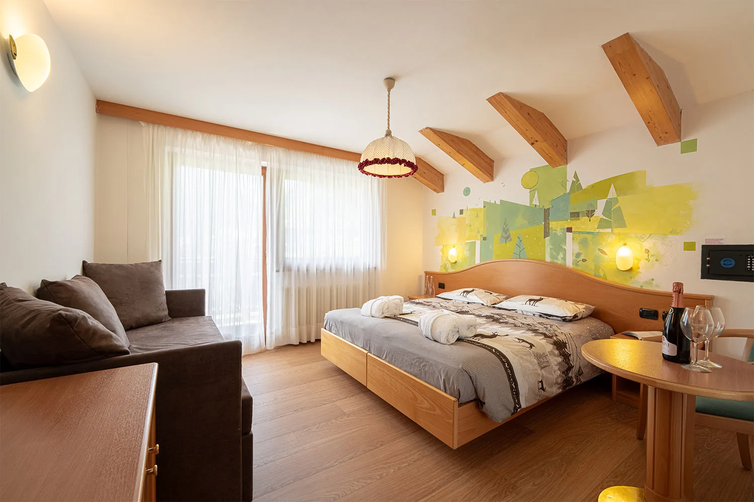 Camera con divano, letto matrimoniale e parete decorata con motivi boschivi