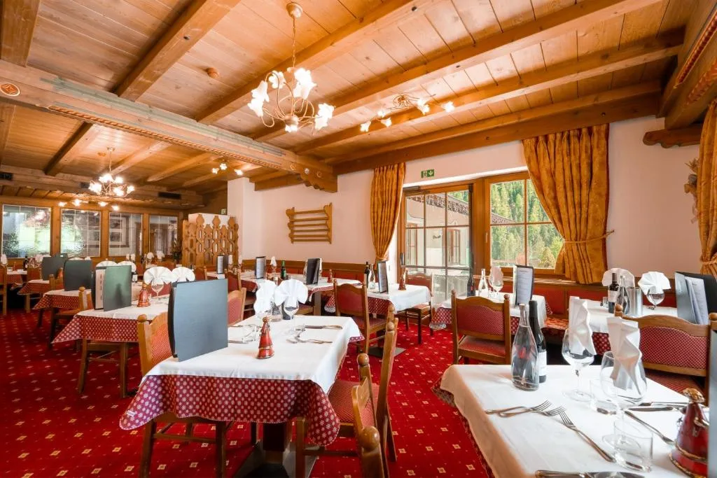 Sala ristorante con tavoli apparecchiati, moquette rossa e soffitto in legno