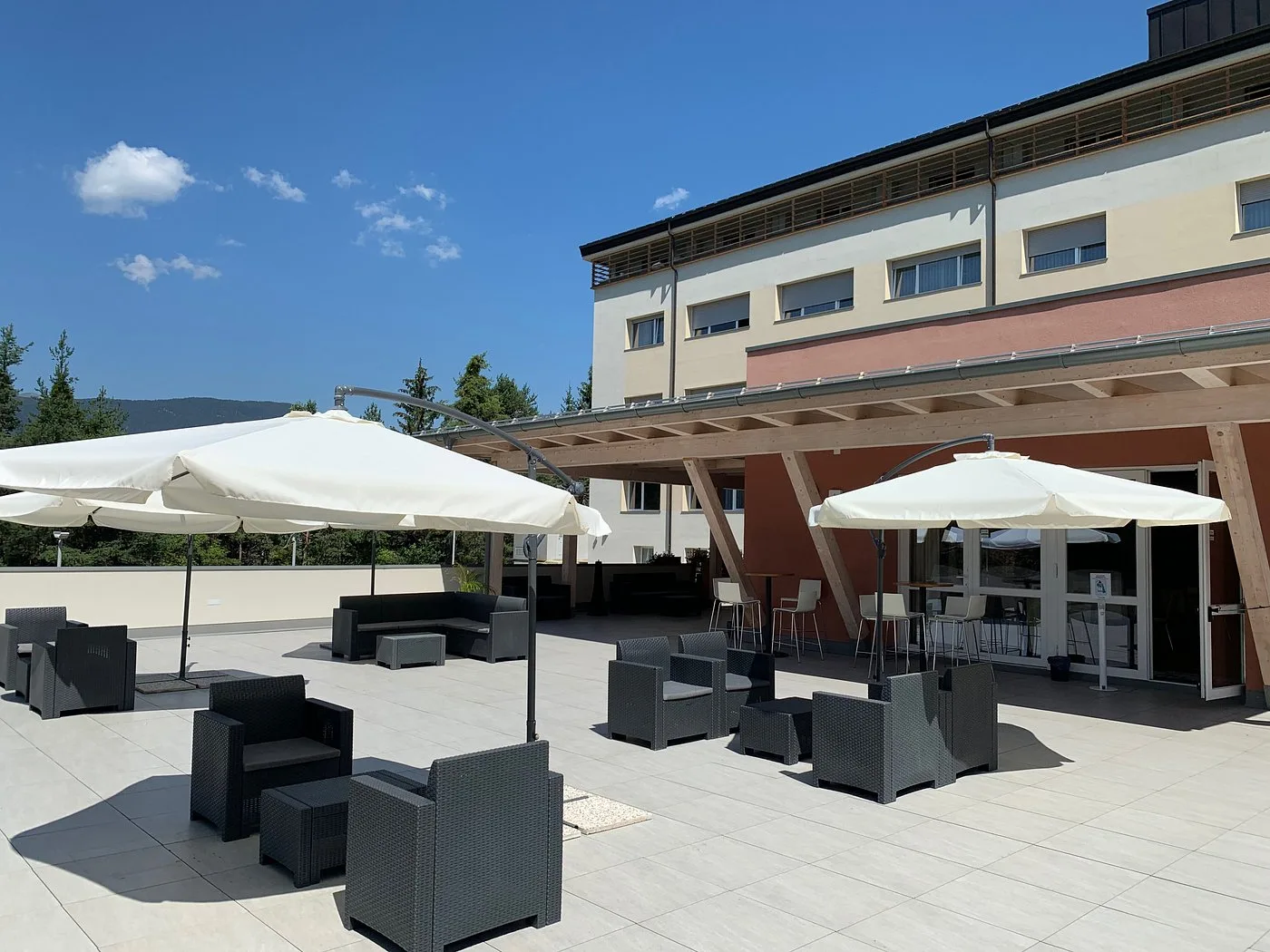 Terrazza esterna con divani in rattan e ombrelloni bianchi in giornata soleggiata