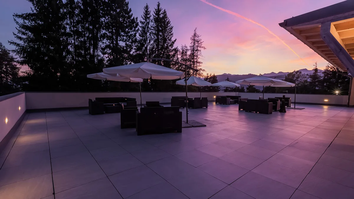 Ampia terrazza con salotti e ombrelloni al tramonto con vista sulle montagne