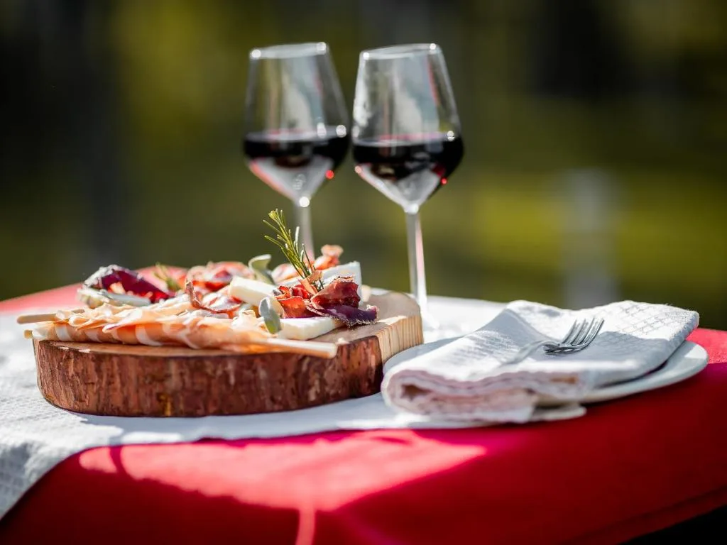 Tagliere di salumi e formaggi con due calici di vino rosso all'aperto