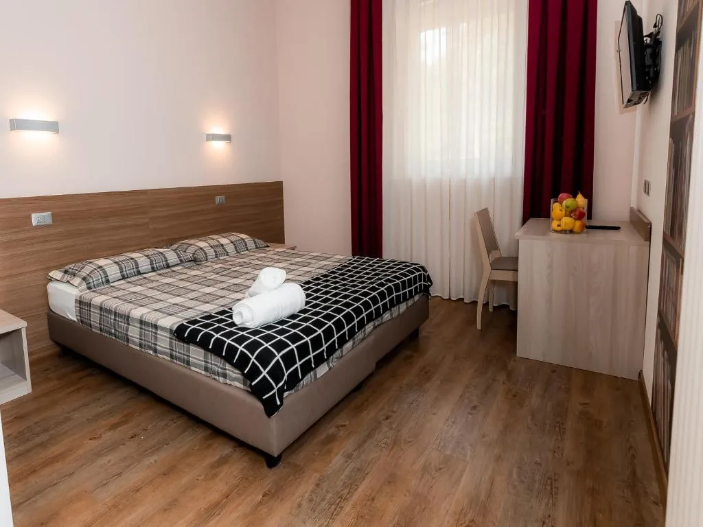 Camera matrimoniale con parquet, tende rosse e scrivania