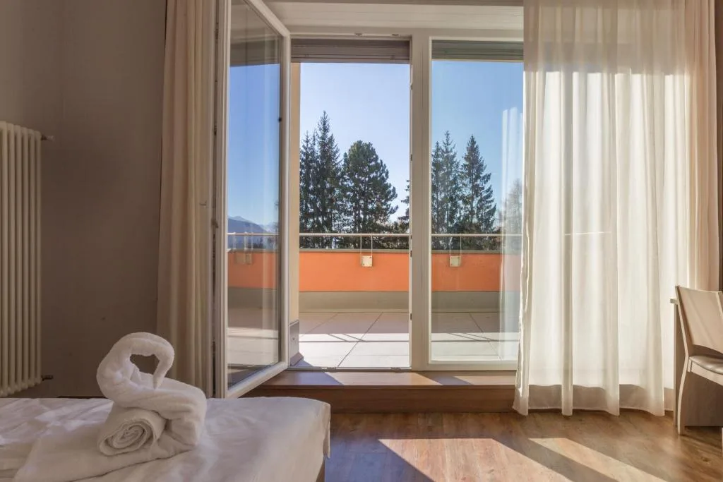 Camera con porta finestra aperta su balcone e vista sugli alberi