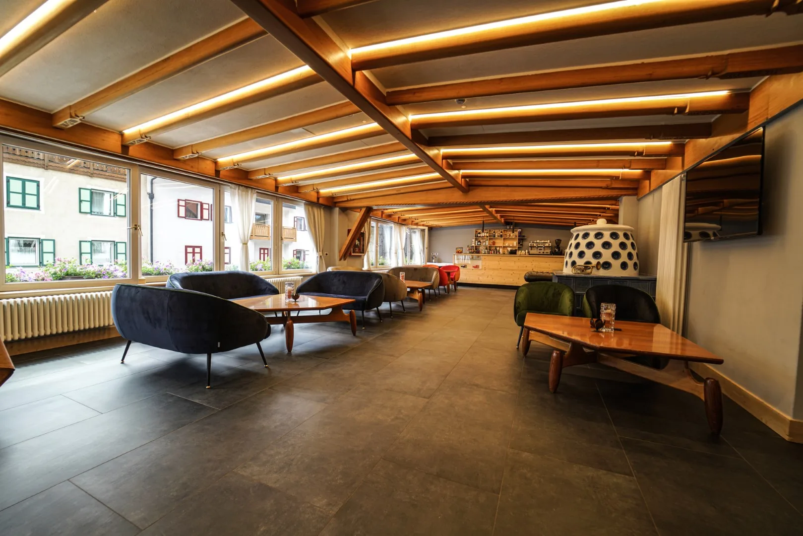 Ampia lounge con poltrone colorate, soffitto in legno illuminato e vetrate sul cortile