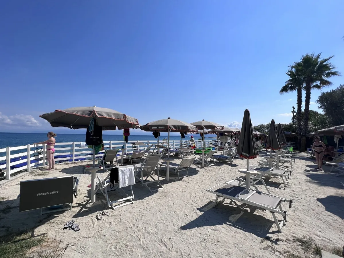 Lido attrezzato con ombrelloni grigi e lettini sulla sabbia in riva al mare