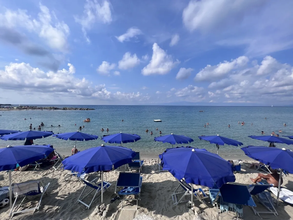 Ombrelloni blu e lettini sulla sabbia con bagnanti nel mare calmo