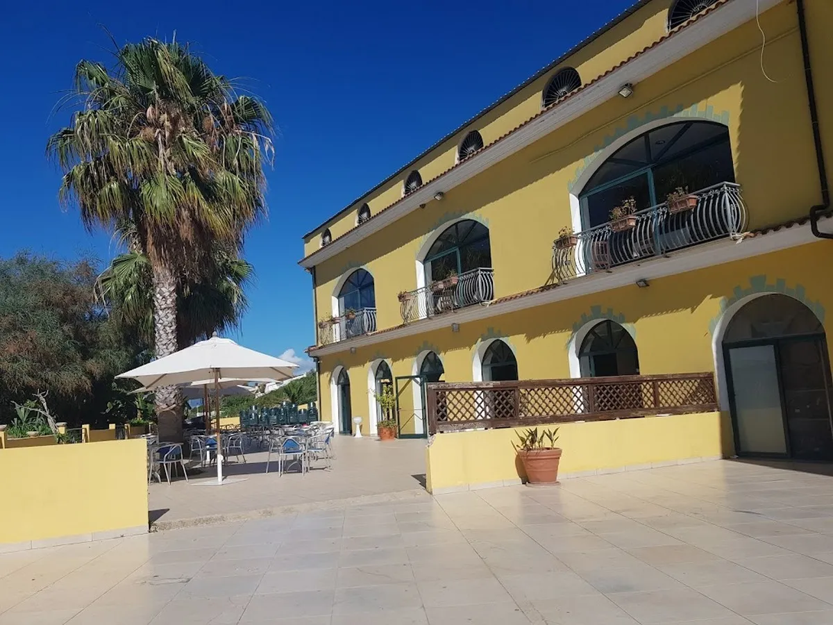Edificio giallo con archi, palma e terrazza esterna con tavoli