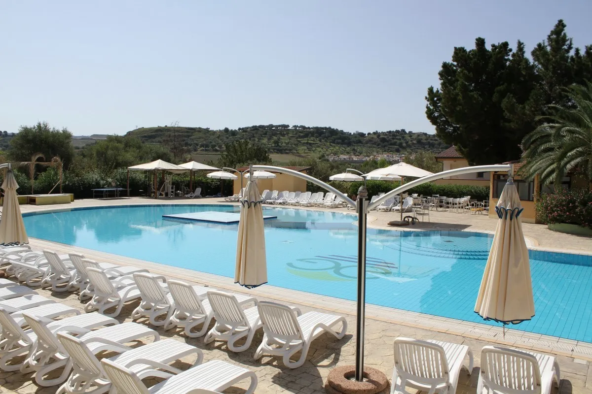 Piscina con lettini bianchi e ombrelloni con vista sulle colline