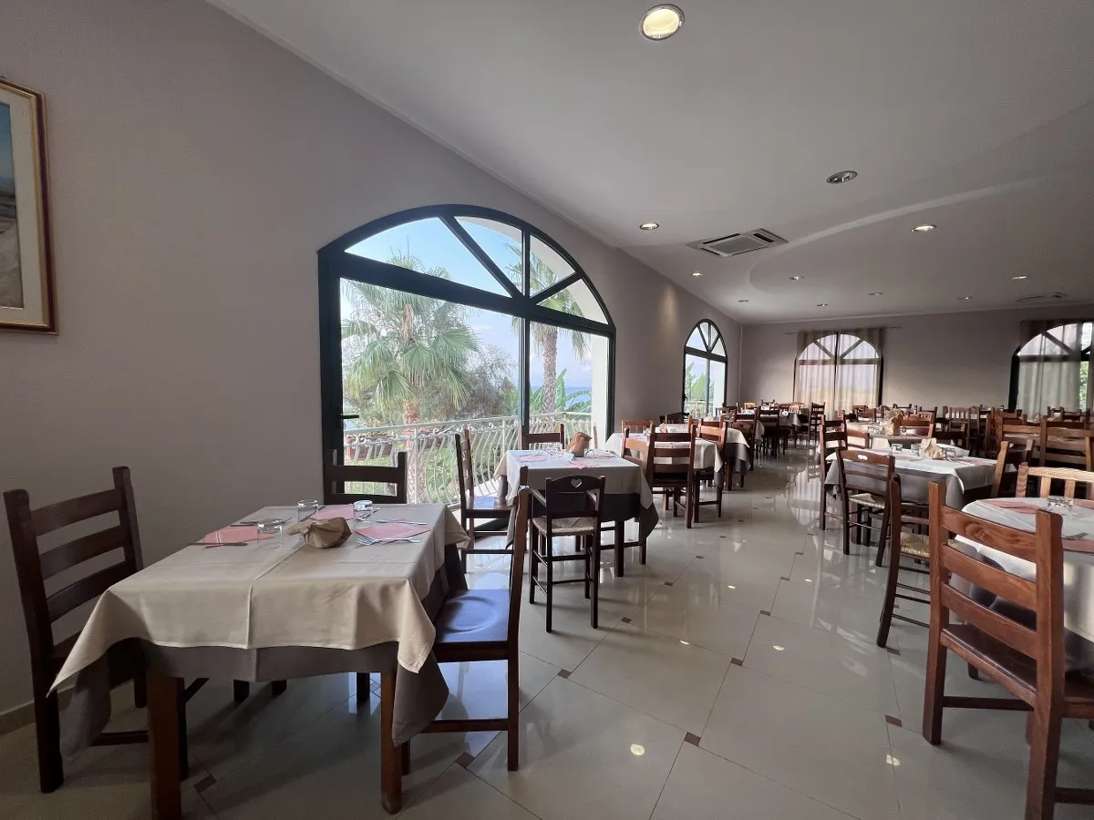 Sala ristorante con tavoli in legno e grandi finestre ad arco con vista
