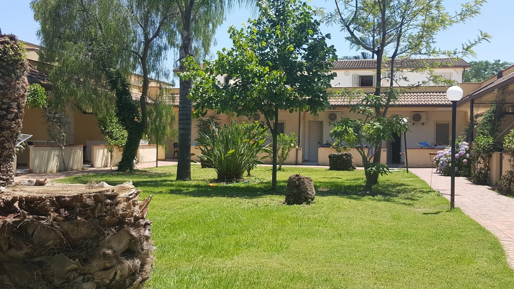 Giardino interno con prato verde, alberi e bungalow gialli
