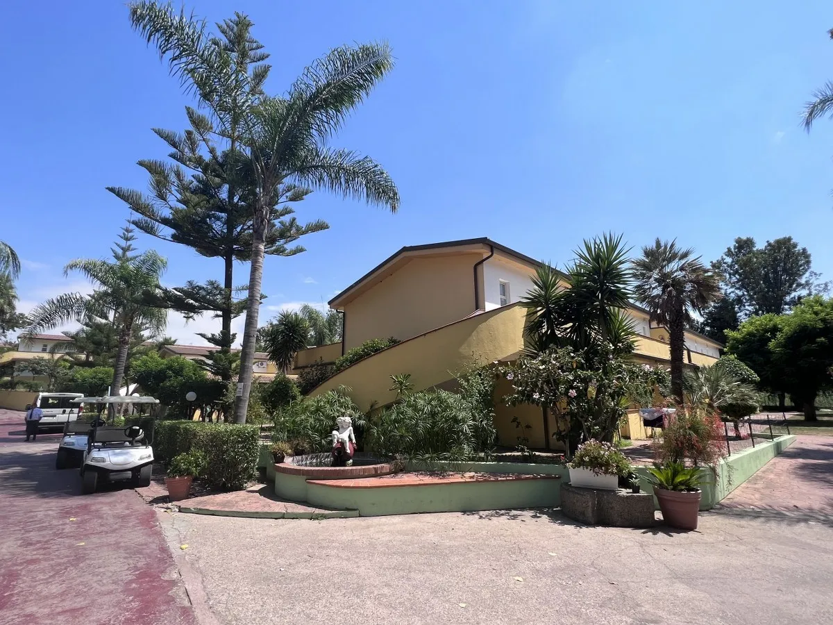 Edificio giallo a due piani con palme, fontana e vialetto