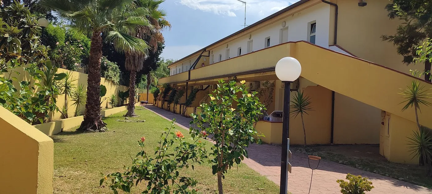 Esterno di edificio giallo con giardino, palme e portico