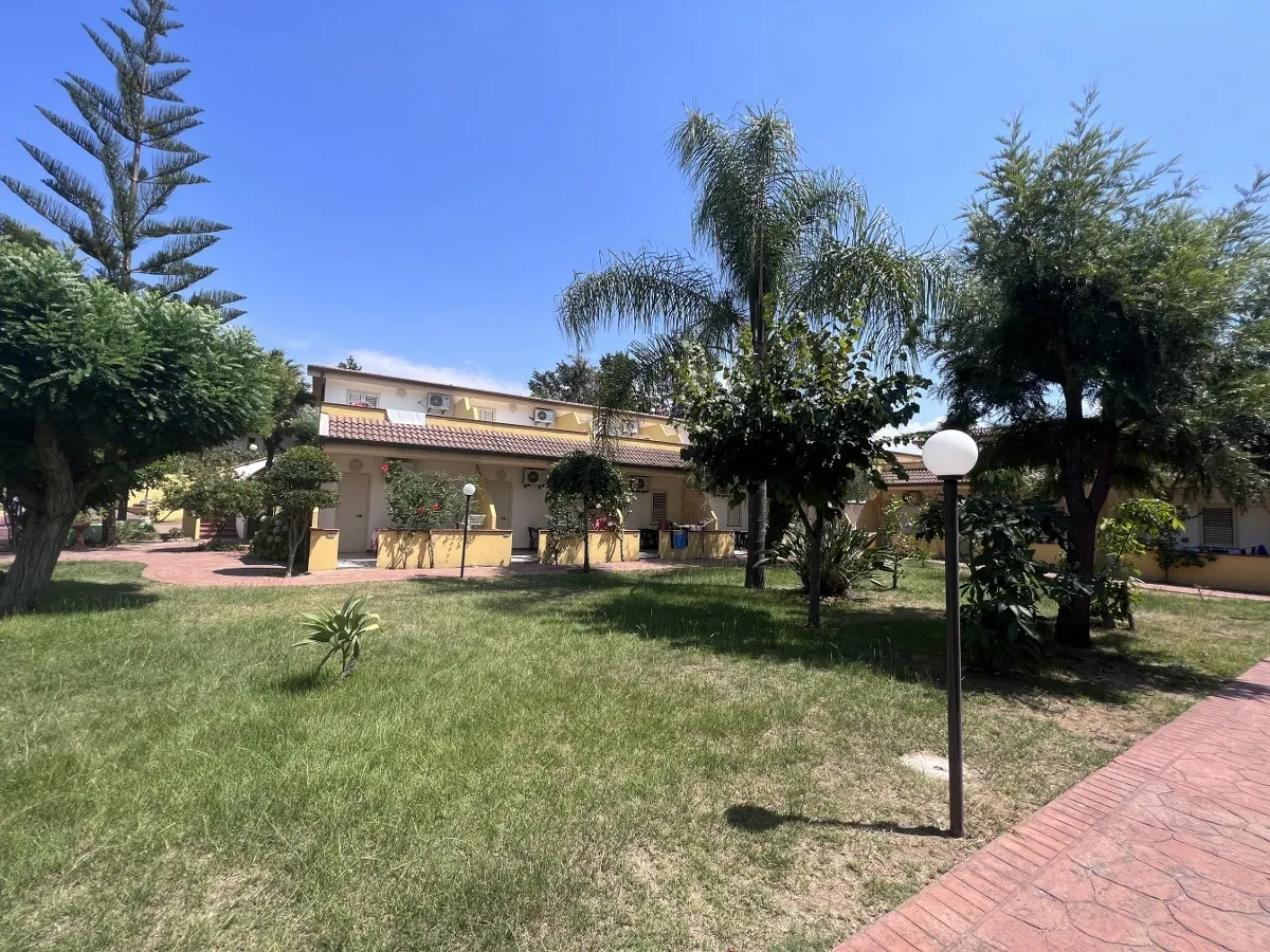 Giardino con prato verde, alberi e bungalow gialli del villaggio