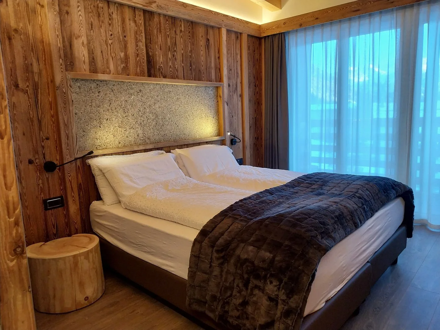 Camera moderna con boiserie in legno, letto matrimoniale e comodino in tronco naturale