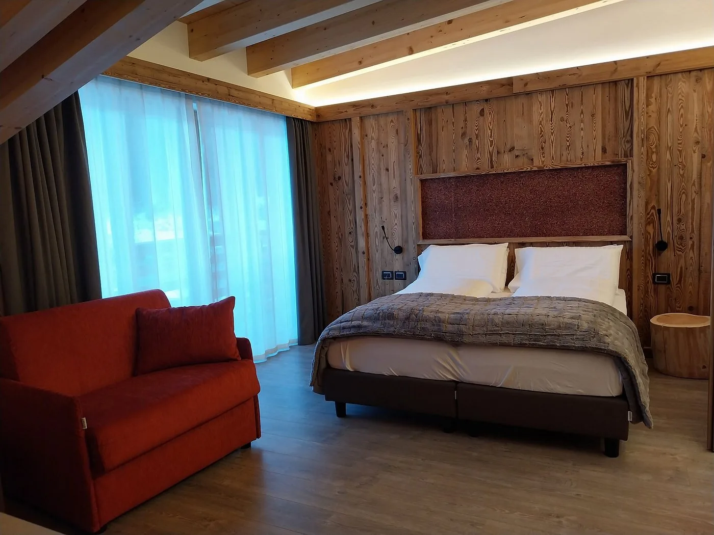 Camera elegante con pareti in legno, letto matrimoniale, divanetto rosso e ampia finestra