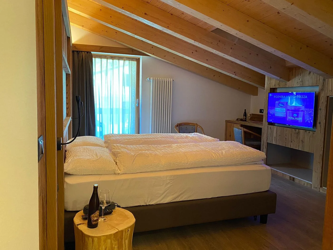 Camera mansardata moderna con travi in legno, letto matrimoniale e TV a parete