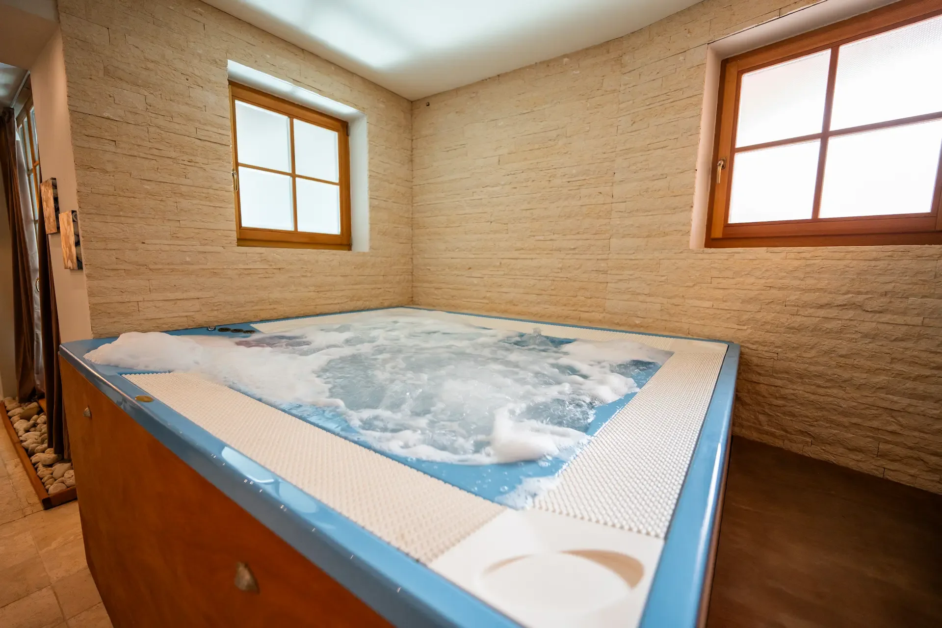 Vasca idromassaggio nell'area wellness con pareti rivestite in pietra e finestre in legno