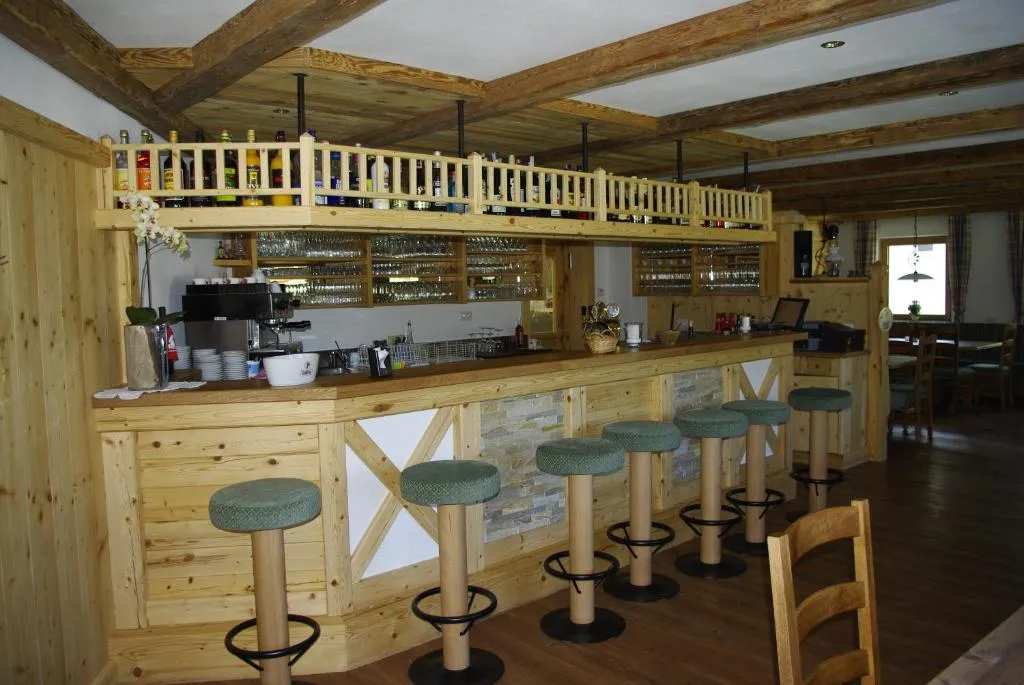 Bancone bar in legno con sgabelli e bottiglie disposte sopra, in ambiente rustico alpino