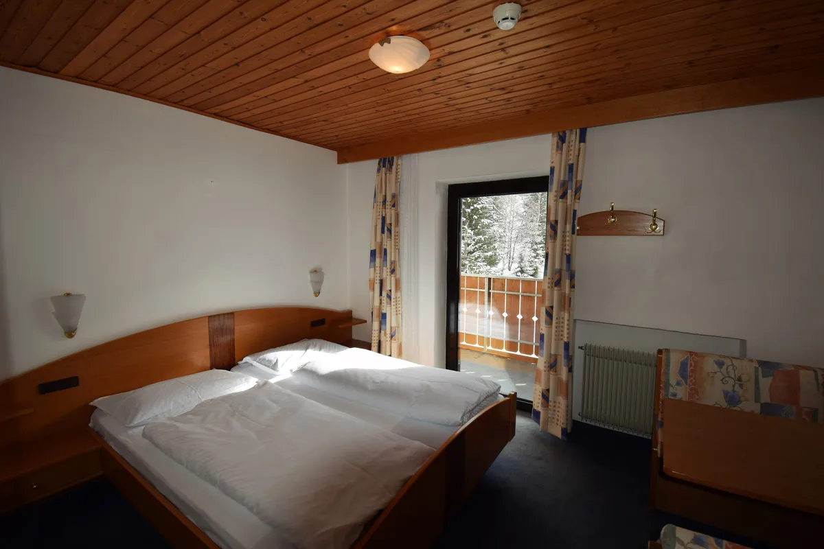 Camera doppia con letto matrimoniale, soffitto in legno e porta finestra con vista sulla neve