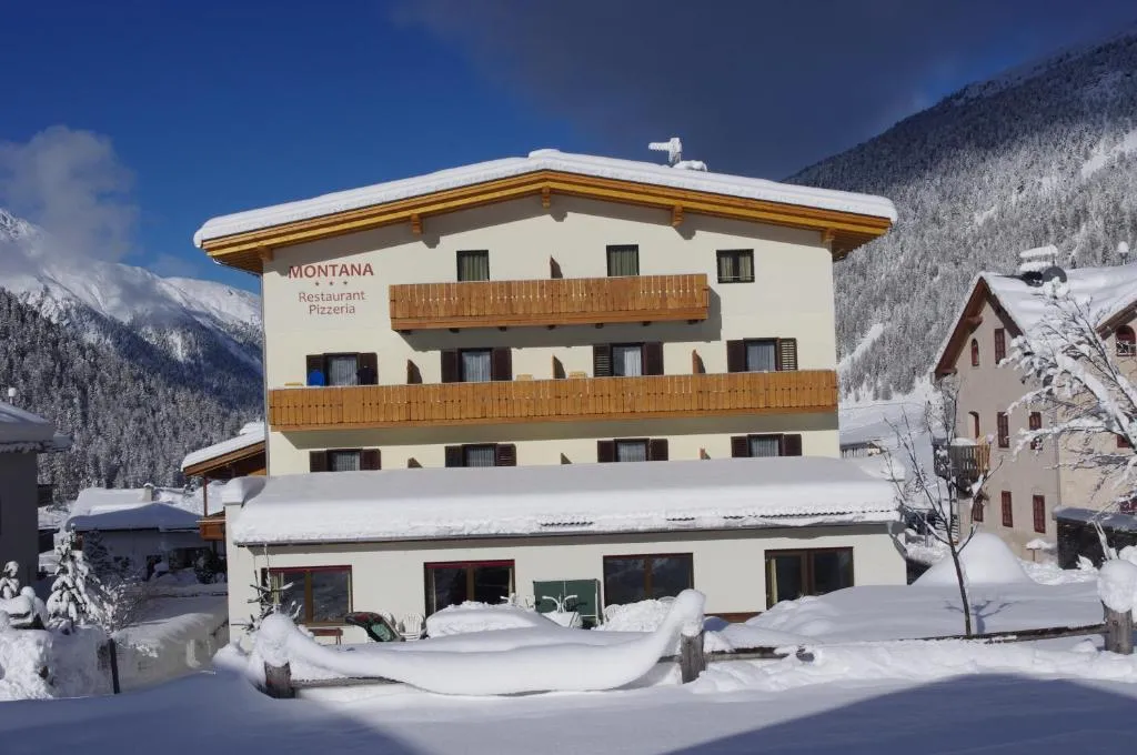 Facciata dell'Hotel Montana coperta di neve con montagne innevate e cielo azzurro