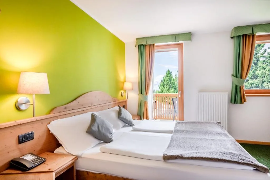 Camera doppia con parete verde, letto in legno e accesso al balcone
