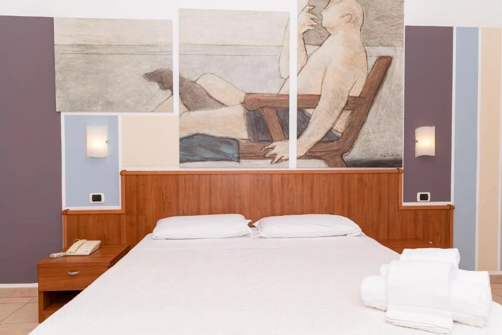 Camera matrimoniale con dipinti alle pareti, letto bianco e comodino con telefono