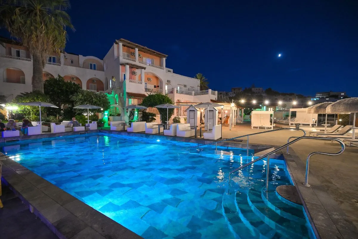 Piscina esterna illuminata di notte con edificio dell'hotel e luna sullo sfondo