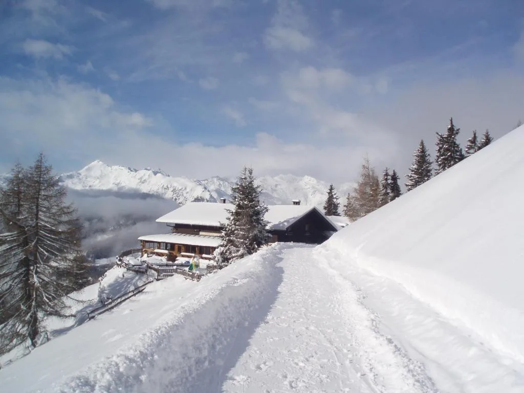 Rifugio di montagna innevato lungo un sentiero con panorama sulle vette alpine in inverno