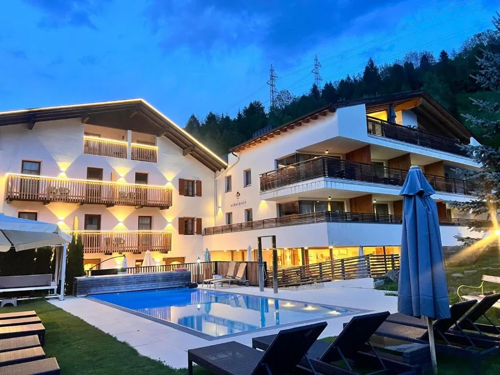 Hotel illuminato di sera con piscina esterna, lettini e ombrelloni al crepuscolo