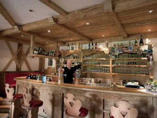 Bar interno in legno rustico con travi a vista, sgabelli e bottiglie esposte sugli scaffali