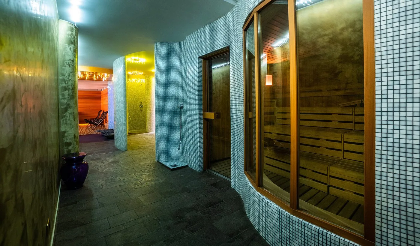 Area saune e bagni rivestita in mosaico con cabina in legno e docce