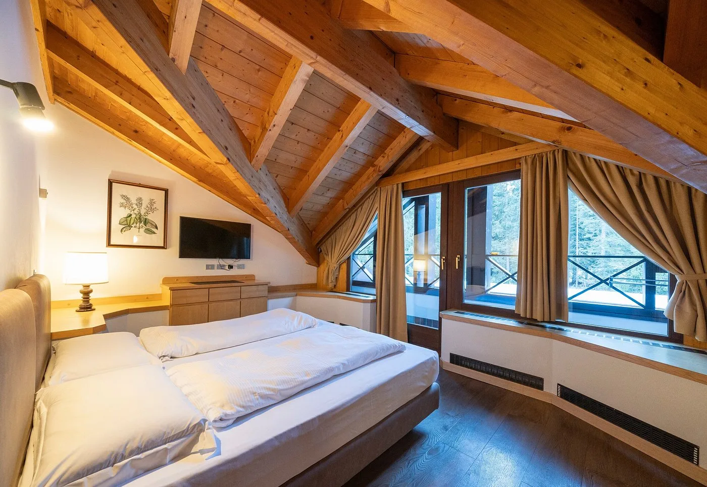Camera mansardata con travi in legno, letto matrimoniale e vista sugli abeti