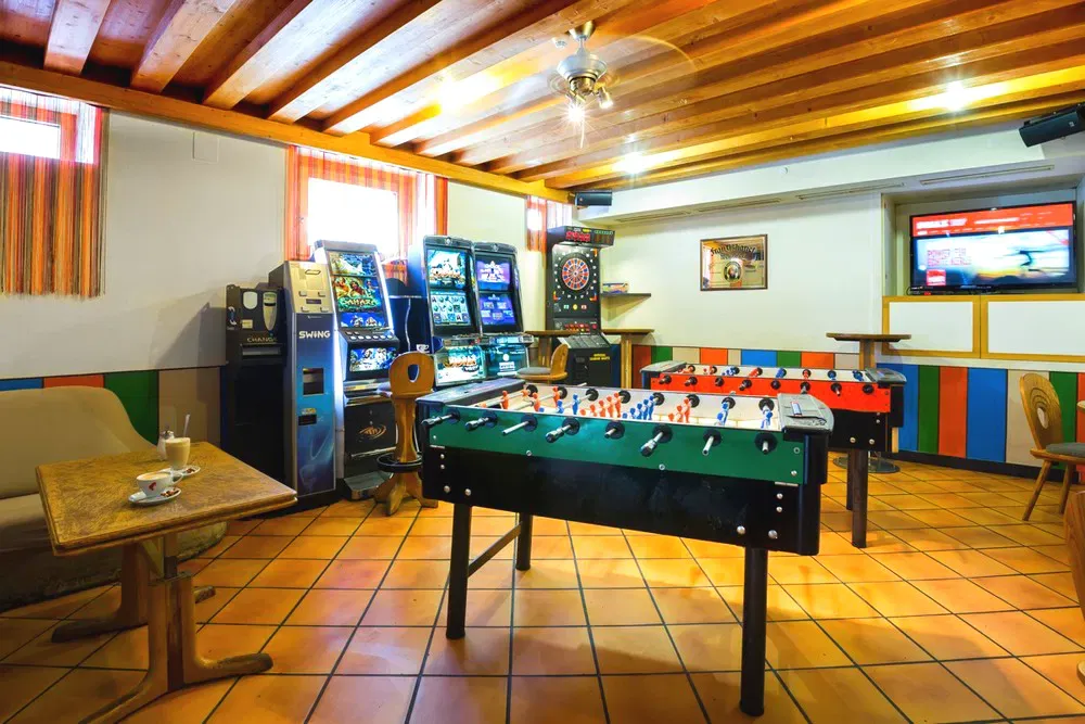 Sala giochi con calcio balilla, slot machine e freccette con soffitto in legno