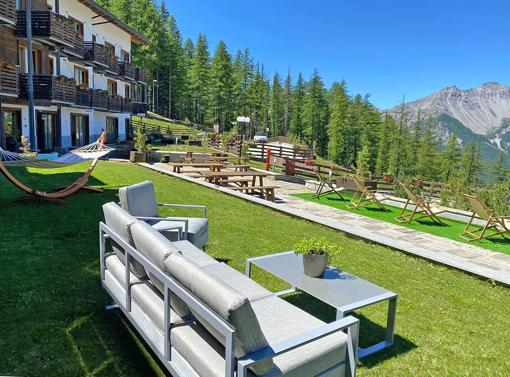 Giardino dell'hotel con divani, amaca e lettini prendisole affacciato sulle montagne estive