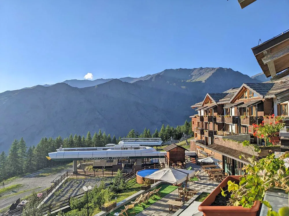 Vista sulle montagne e impianto di risalita dalla terrazza dell'hotel con fiori in estate
