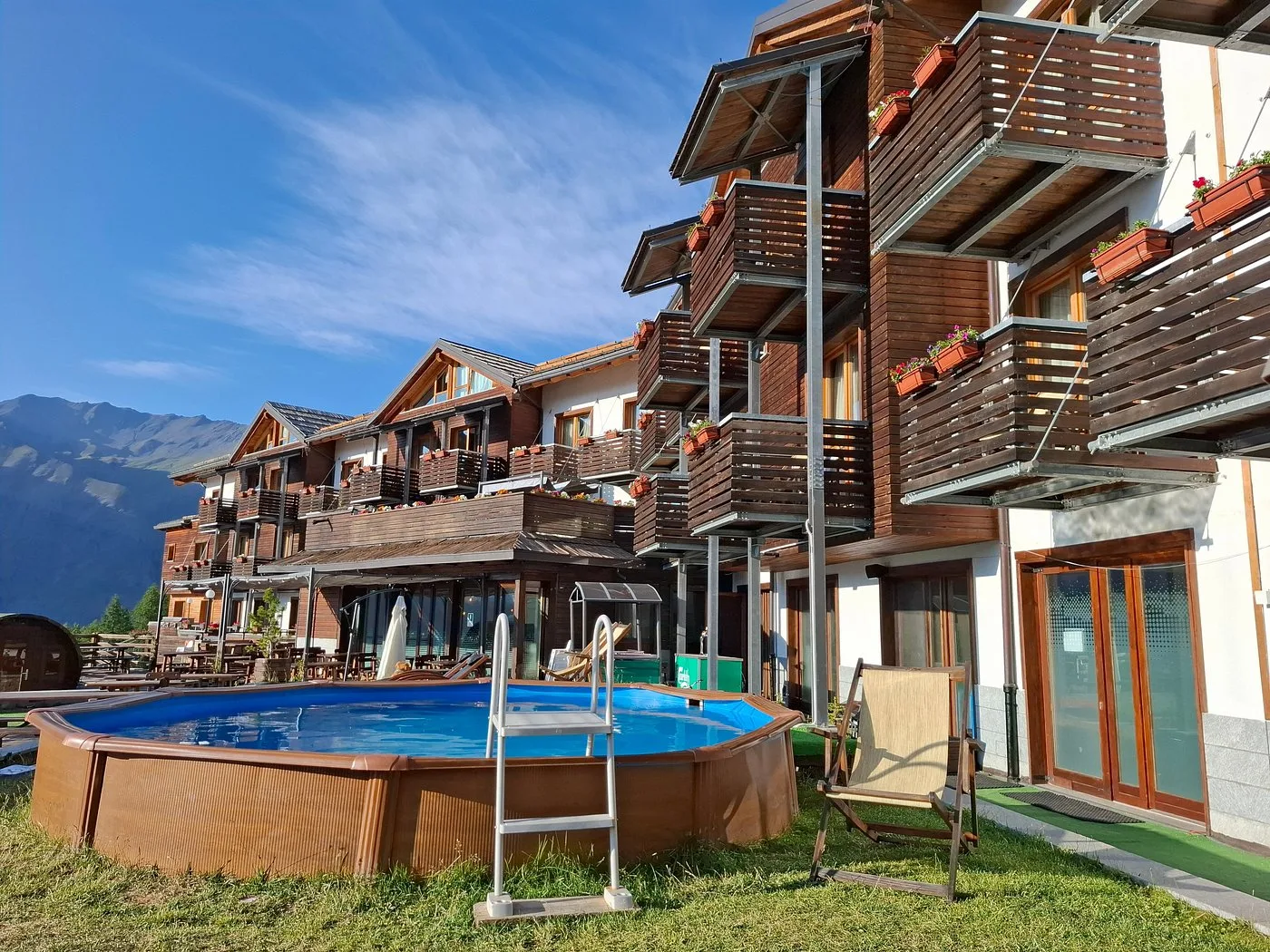 Piscina esterna circolare in legno con sdraio accanto alla facciata dell'hotel
