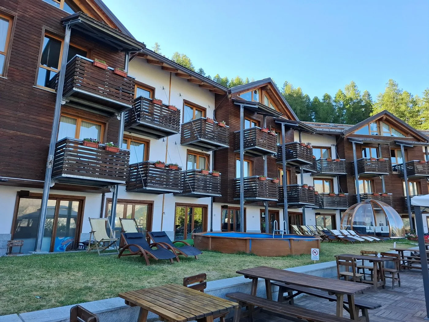 Facciata dell'hotel con balconi fioriti, piscina esterna e area relax nel giardino