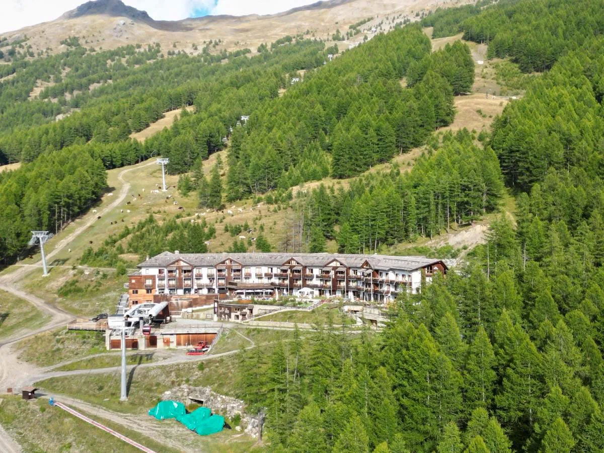 Veduta aerea dell'hotel immerso nel bosco di conifere con impianti di risalita in estate