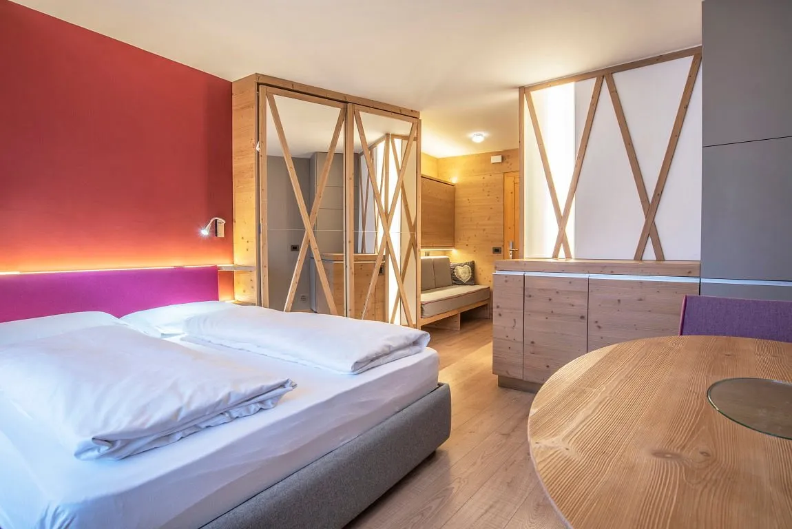 Camera moderna con letto matrimoniale, parete rossa e arredi in legno chiaro