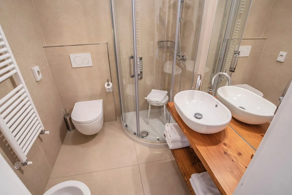 Bagno con doccia curva, doppio lavabo su piano in legno e wc