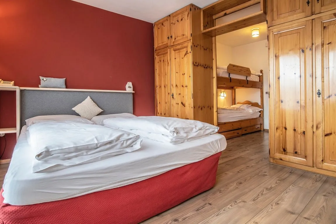 Camera con letto matrimoniale, parete rossa e letto a castello in legno