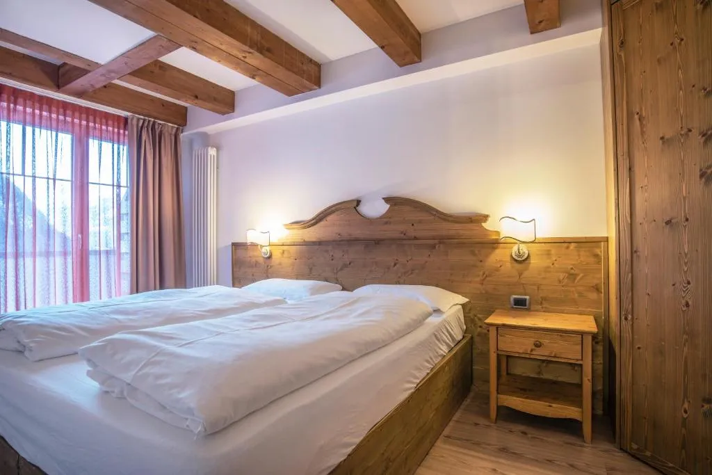 Camera matrimoniale con testiera in legno, comodino e finestra con tende