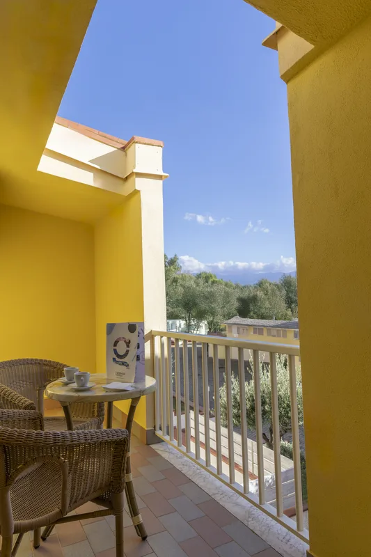 Balcone giallo con tavolino, sedie in vimini e vista sul verde