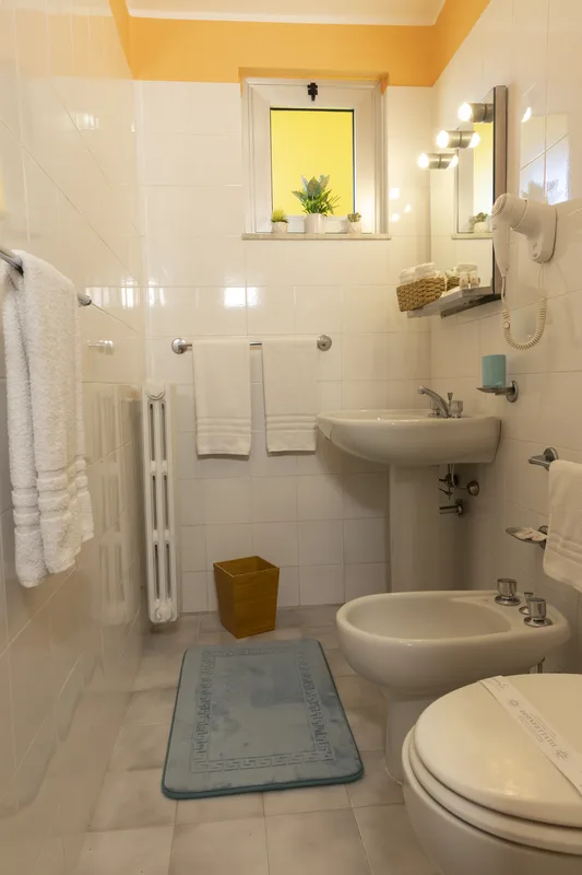 Bagno con piastrelle bianche, lavabo, bidet e finestra luminosa
