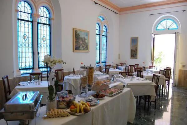 Sala colazione con buffet di frutta e dolci, tavoli apparecchiati e vetrate liberty
